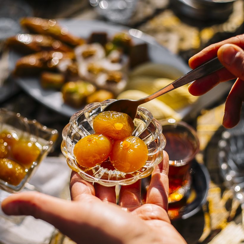 top view of a hand holding a small glass saucer with apricot jam